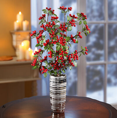 Dekoratives Gesteck mit roten Beeren und gr&uuml;nen Zweigen in einer silberfarbenen Vase auf einem Holztisch