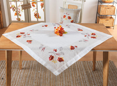 Wei&szlig;e Tischdecke mit herbstlichen Bl&auml;ttern und Zweigen in Rot, Orange und Braun auf einem Holztisch